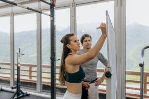 A woman and a man write on a whiteboard to design a weight training routine